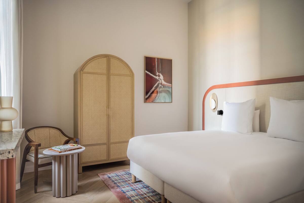 Habitación de hotel con una cama grande, una mesita redonda con un libro, una silla de mimbre y un armario.