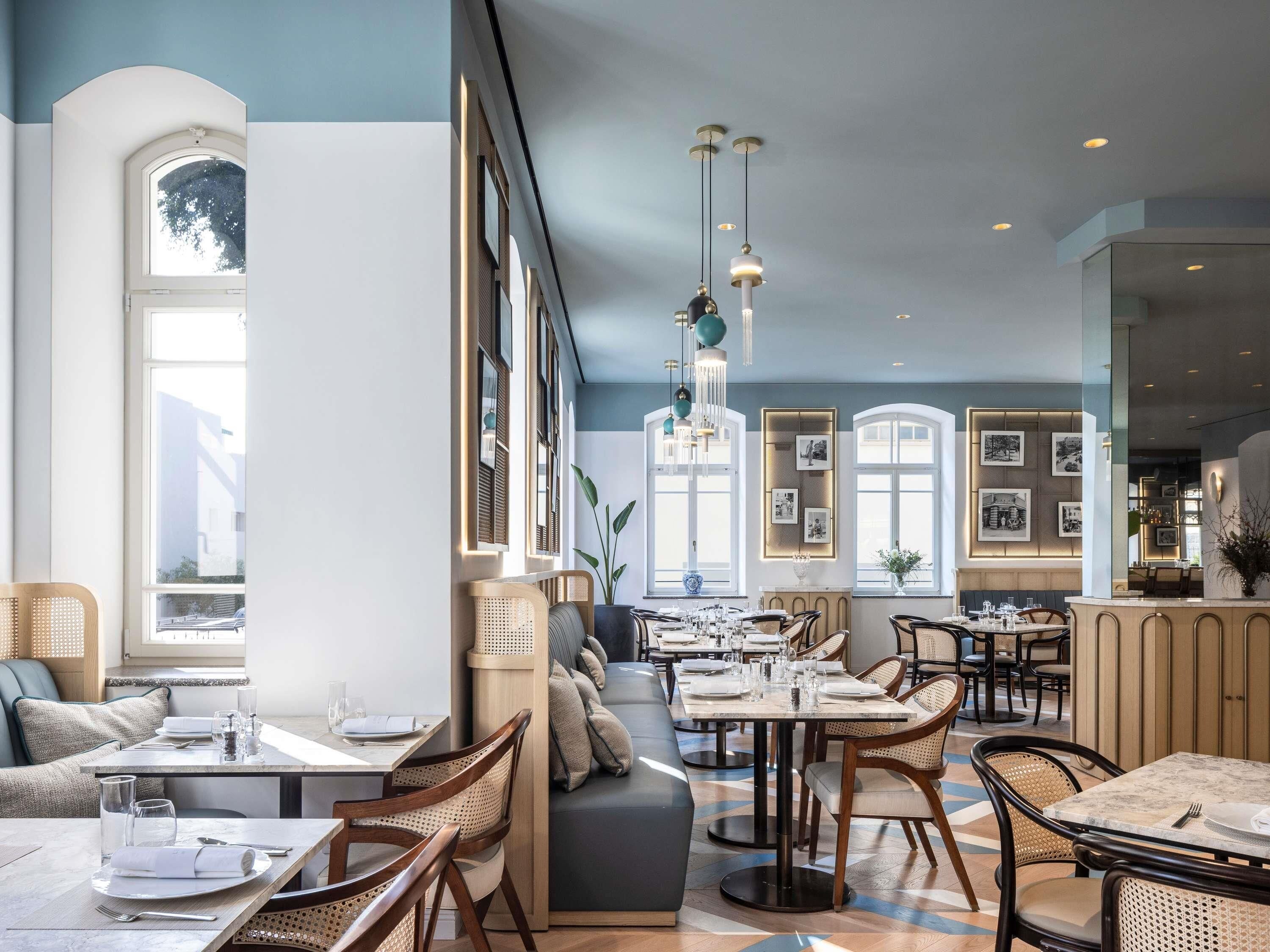 A restaurant with high ceilings, pendant lighting, and a mix of seating including tables and a bench.