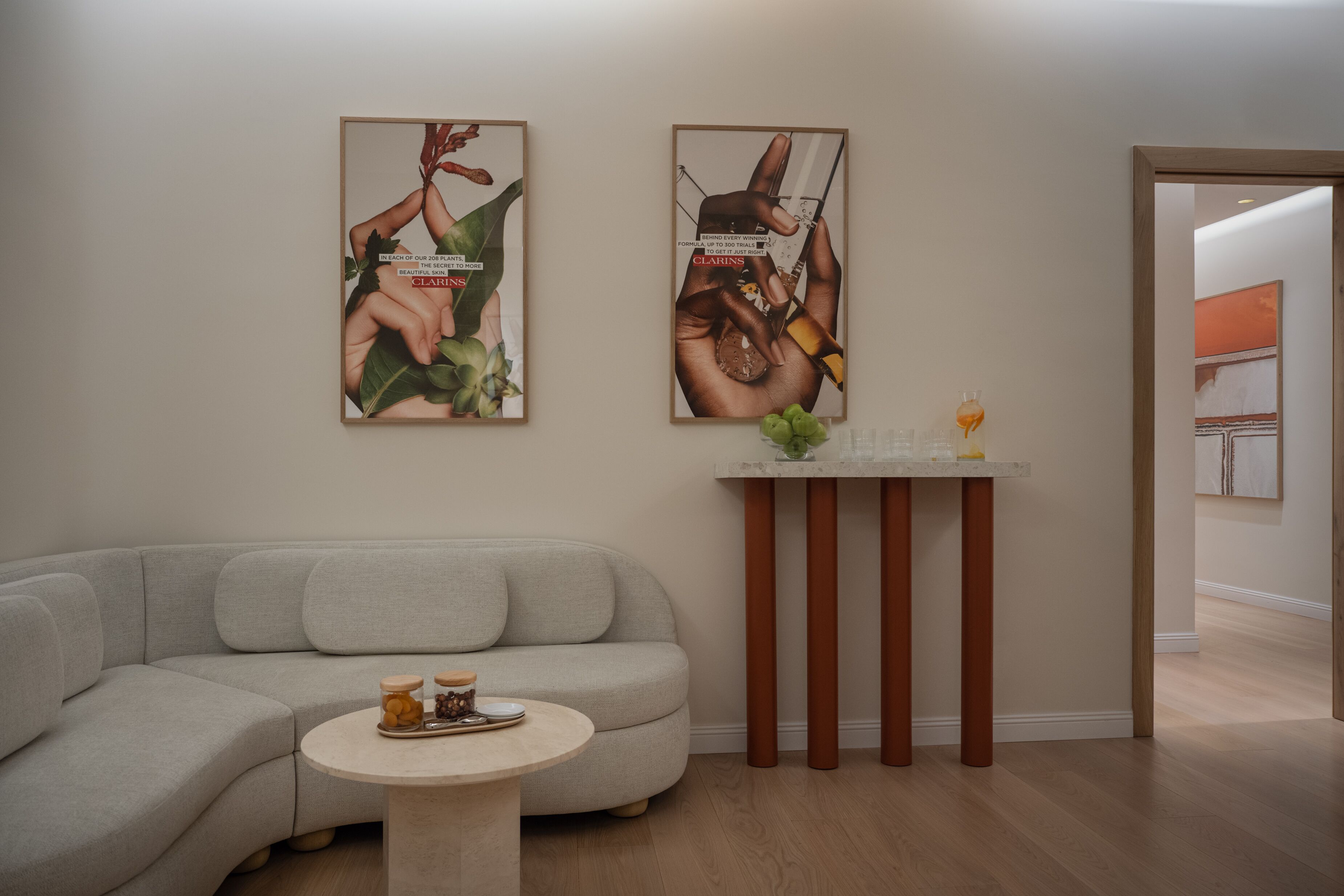 Un salon moderne avec un canapé gris, une petite table ronde sur laquelle sont posés un vase et un plateau, et deux affiches encadrées accrochées au mur.