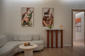 A modern living room with a grey sofa, a small round table with a vase and a tray, and two framed posters on the wall. - Elkonin Tel Aviv - MGallery (Tel Aviv)