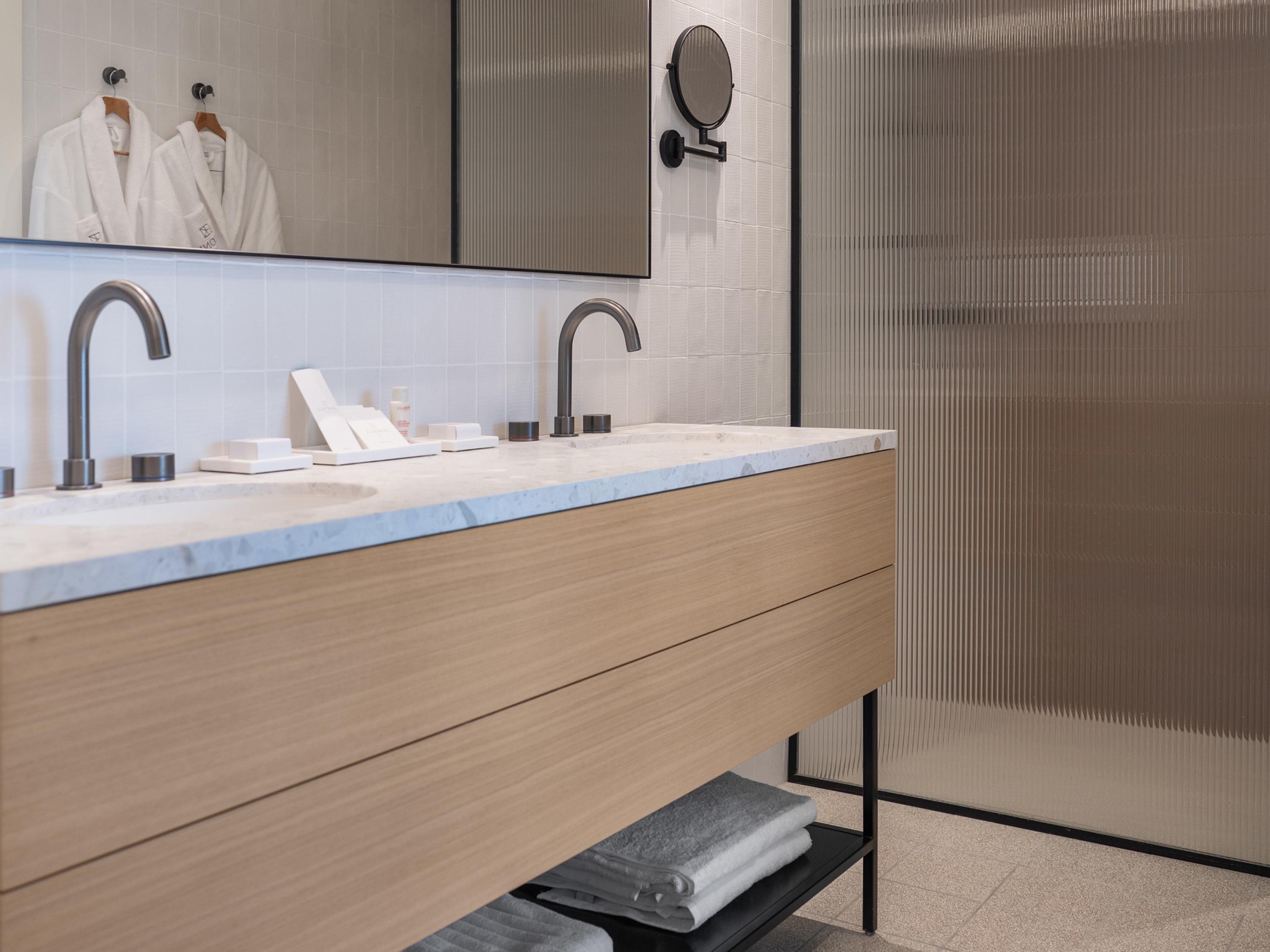 A modern bathroom with a double sink, wooden vanity, and a large mirror.