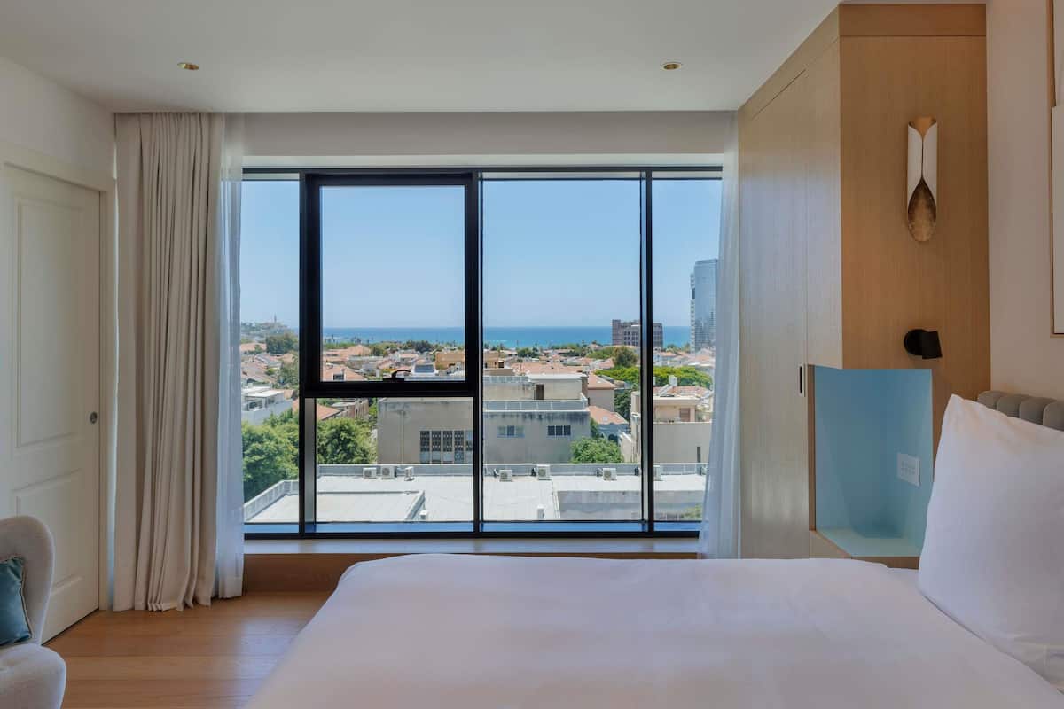 Una camera d'albergo con una grande finestra, un letto, una sedia e una scrivania.