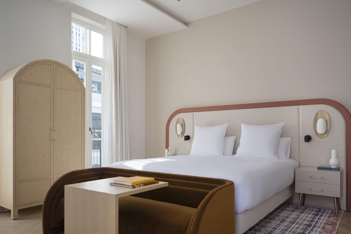 Una camera d'albergo con un letto, comodini, un armadio e un tavolino con libri.