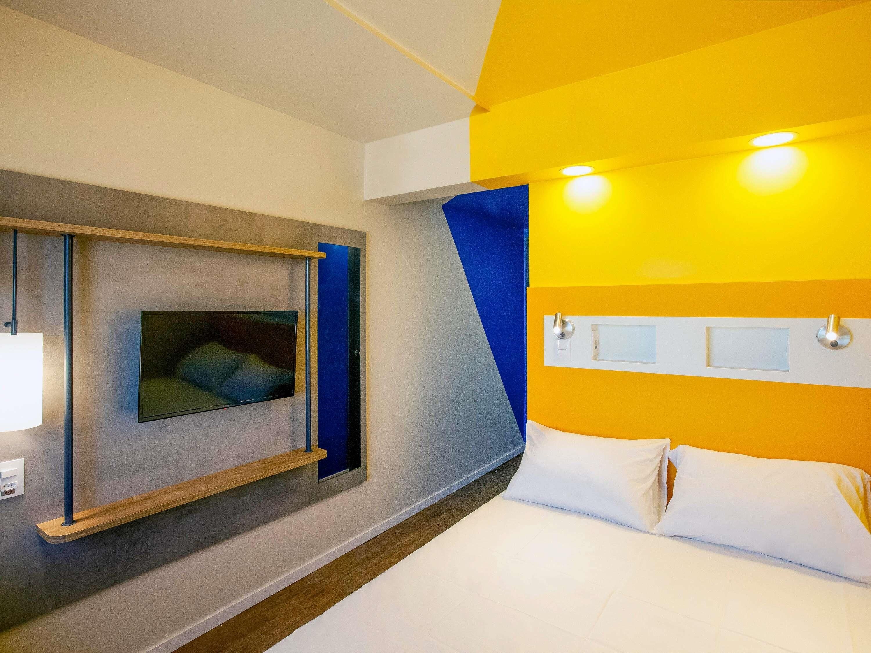 A hotel room with a bed, a mounted television, and a bedside table.