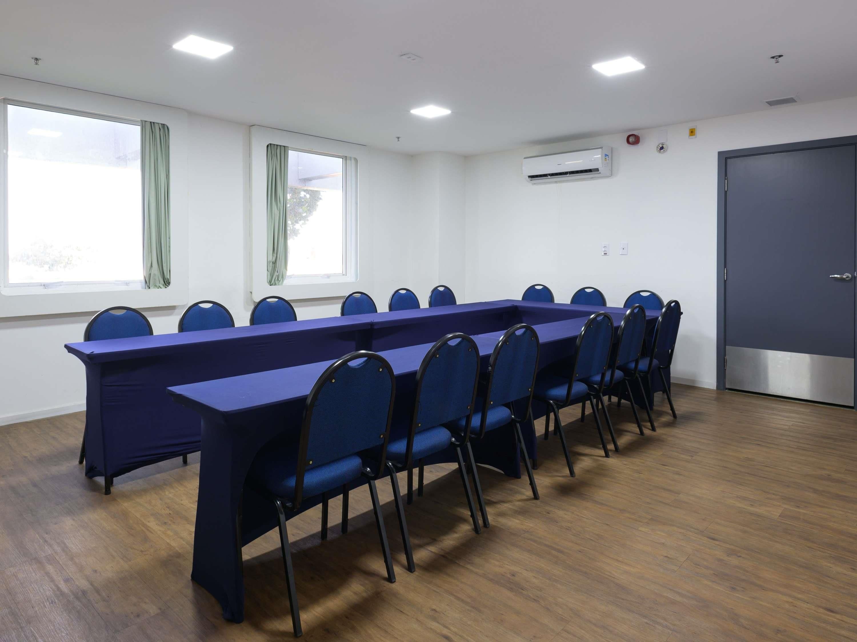 Una sala de conferencias con una larga mesa, sillas, ventanas, un equipo de aire acondicionado y una puerta.