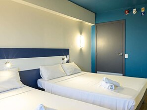 Una camera d'albergo con due letti, una porta scura e un punto luce fissato al muro.