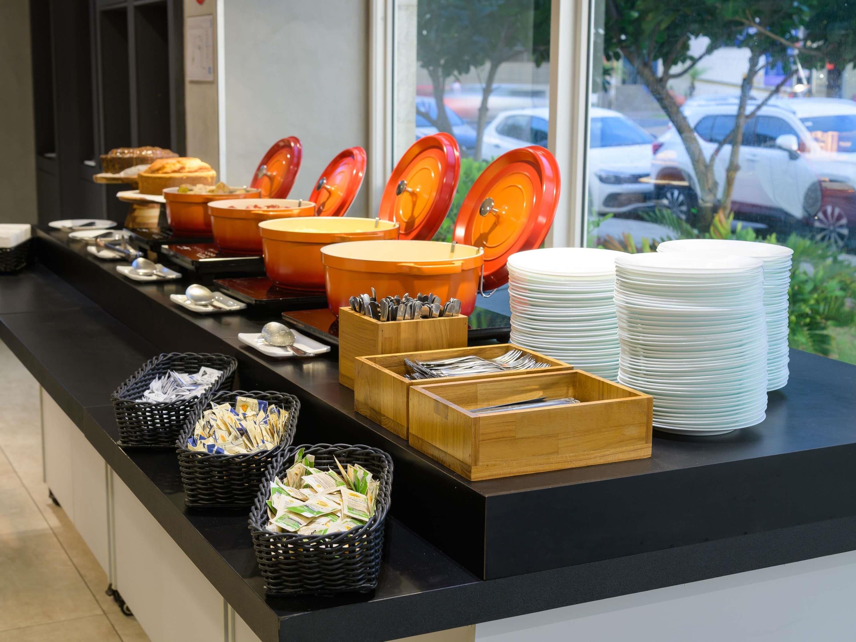Un buffet avec différents récipients contenant de la nourriture, des ustensiles et des assiettes empilées.