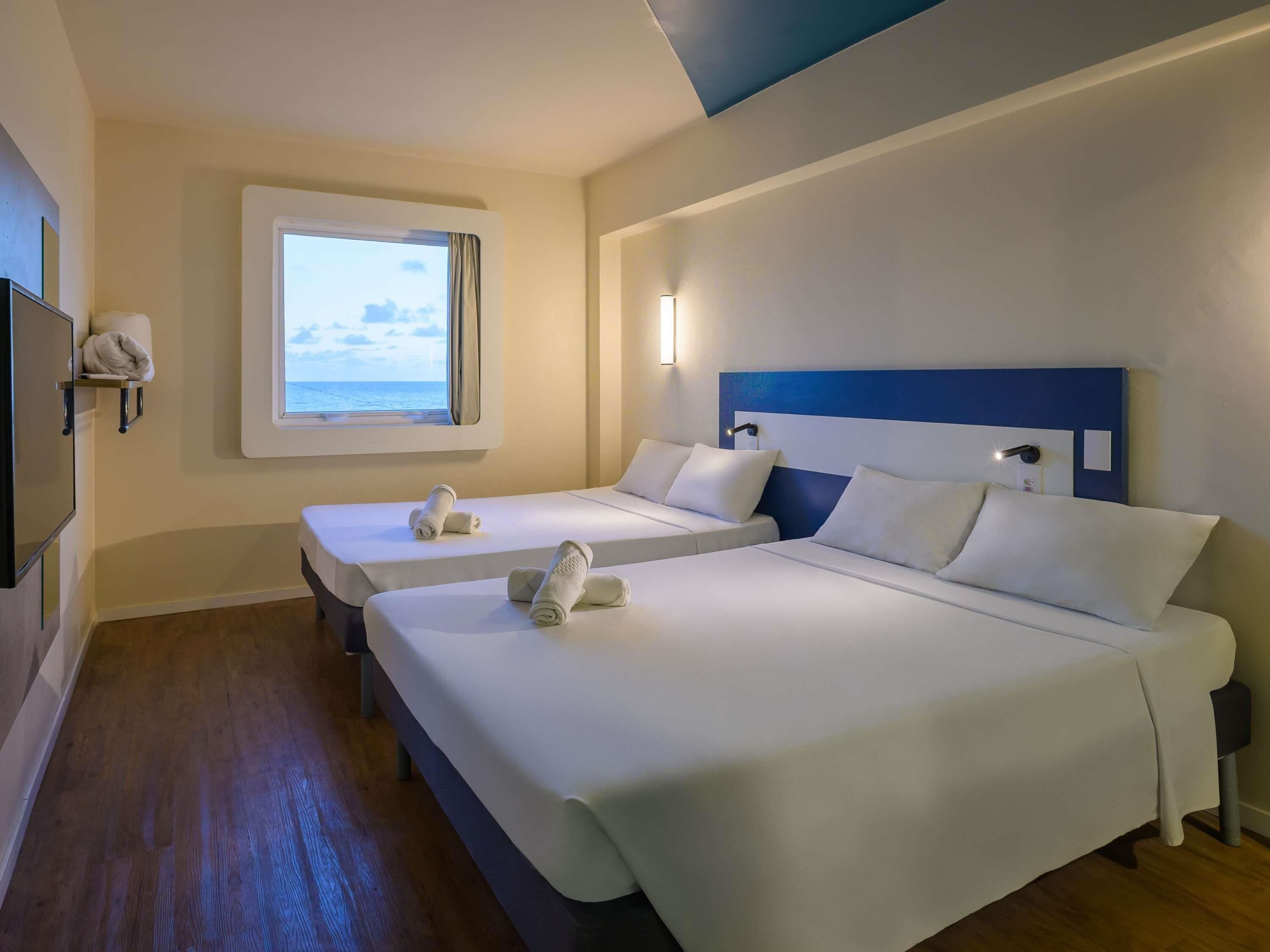 Habitación de hotel con dos camas, una ventana con vistas, un televisor de pantalla plana y una mesita de noche con lámpara.