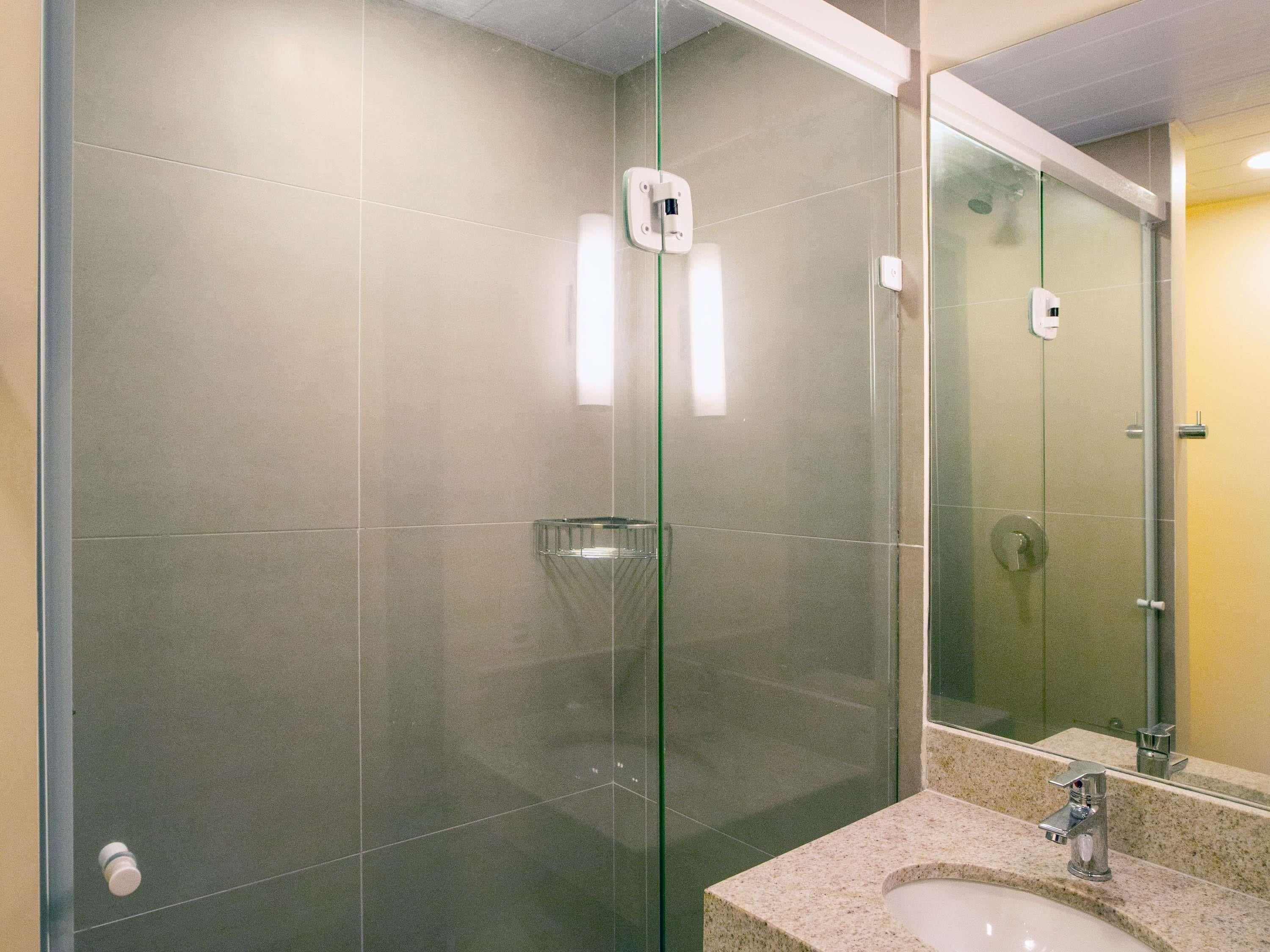 A modern bathroom with a glass shower enclosure, a granite countertop sink, and a large mirror.