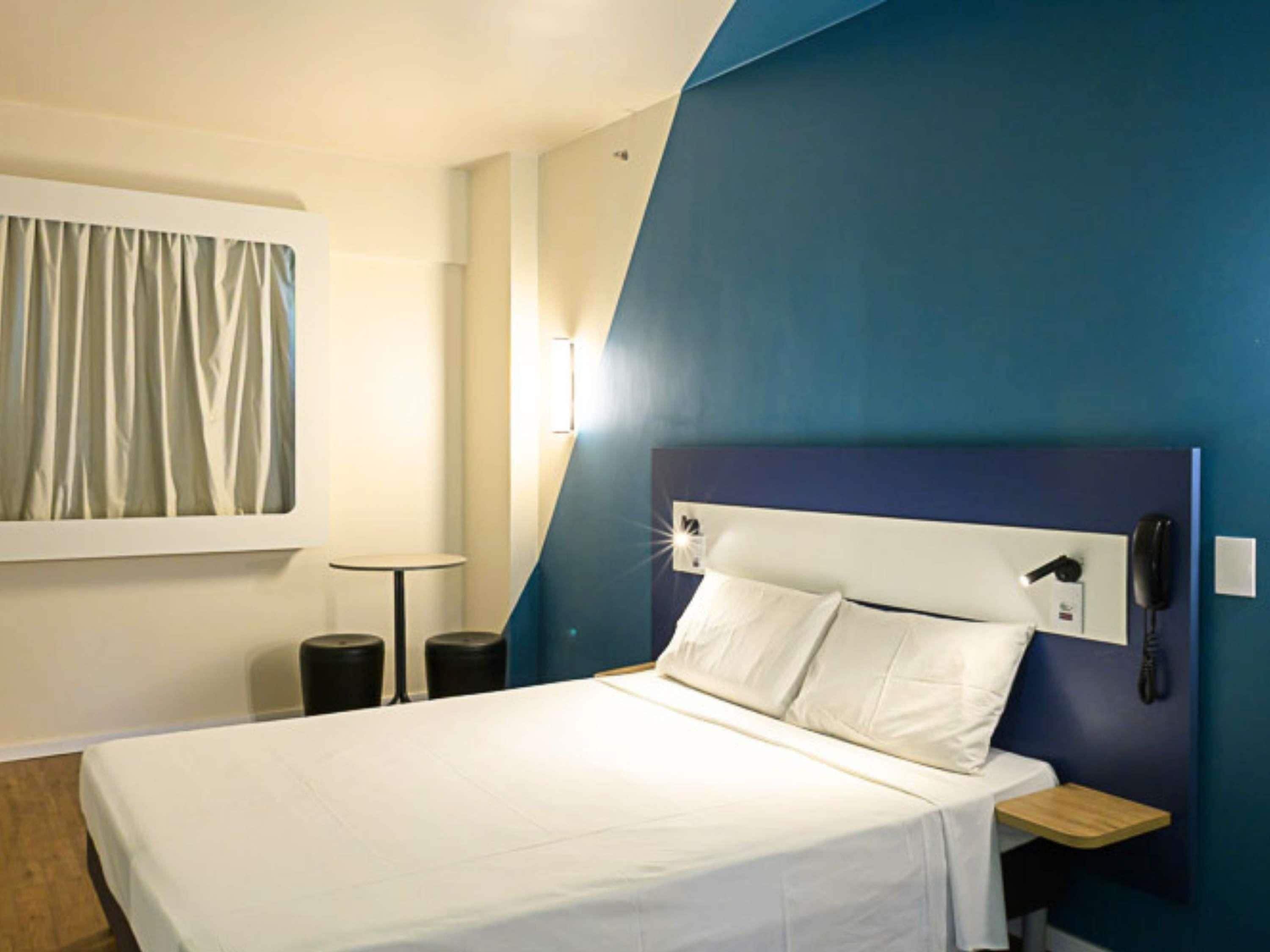 A hotel room with a bed, bedside table, nightstand, and a telephone.