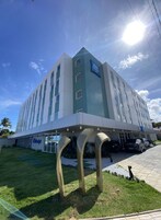 Um hotel moderno com um sinal de 'ibis budget' bem visível, entrada coberta e área de estacionamento com carros.