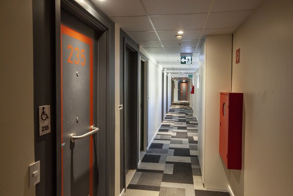 A hotel corridor with a checkered floor, a fire alarm, and a wheelchair accessibility sign. - ibis budget Recife Jaboatão (Jaboatão dos Guararapes)