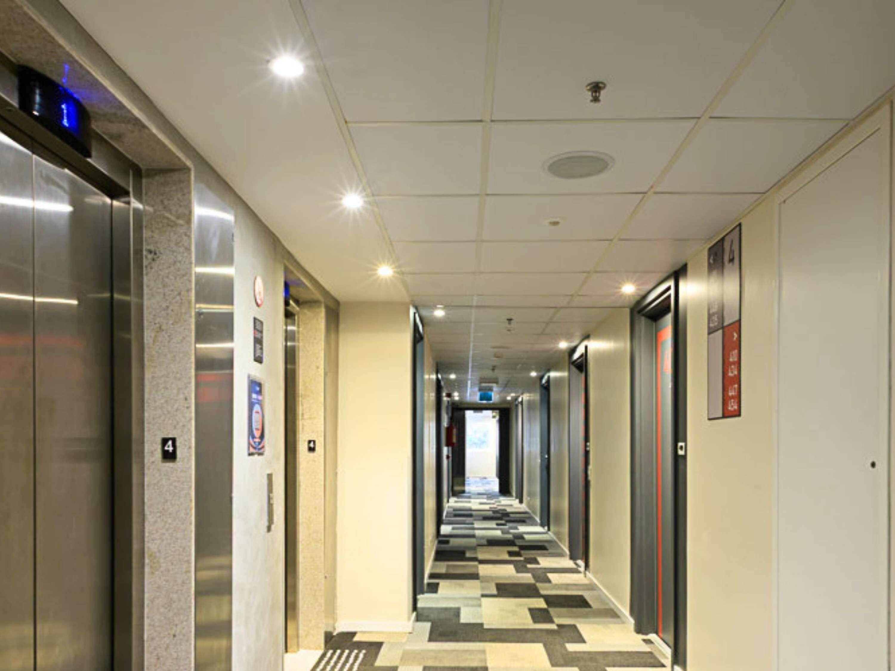 Un pasillo de hotel con ascensores, piso estampado e iluminación empotrada en el techo.
