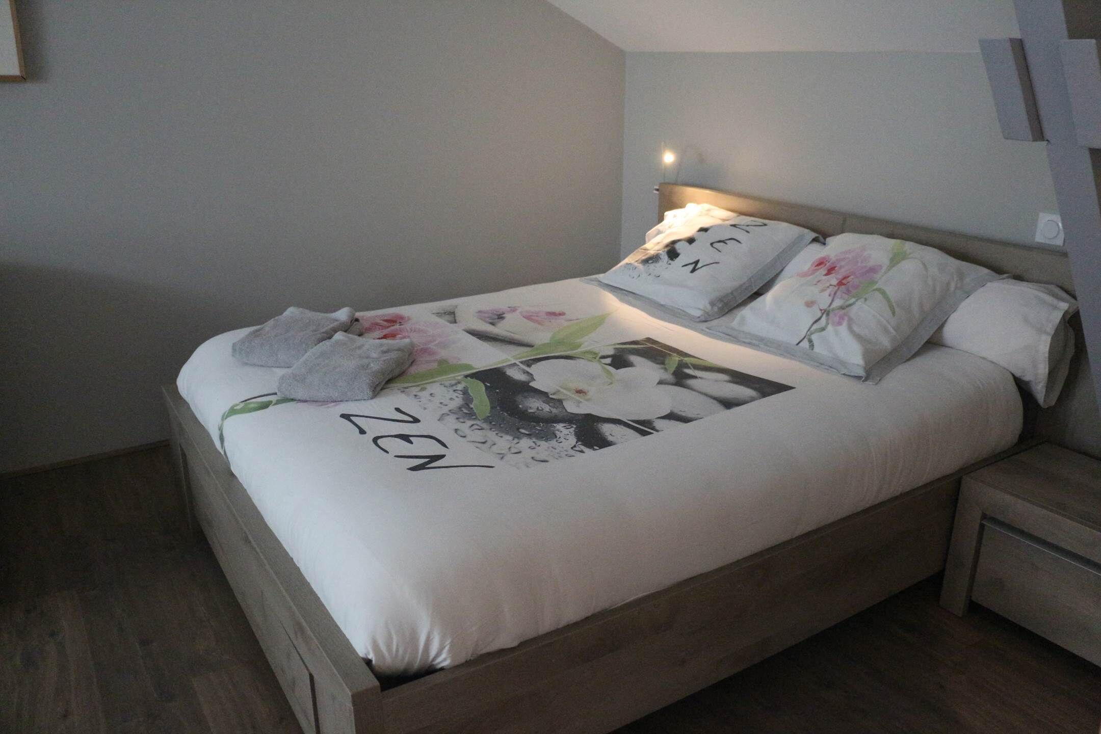 Ein ordentlich bezogenes Bett mit floralem Überwurf, ein Kopfkissen mit Blumenmuster und ein Handtuch auf der Seite.