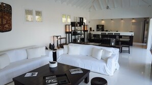 A modern living room with a white sofa, a dark coffee table, and a dining area with a black and white color scheme.