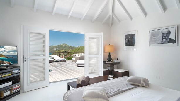 A bedroom with a bed, a desk, a TV, and a view of a deck with outdoor furniture.