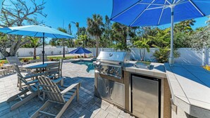 An outdoor patio with a grill, seating, and umbrellas. - Wave n Sea - Close to the Beach with Pool - Anna Maria Island - By Island Real E (Anna Maria)