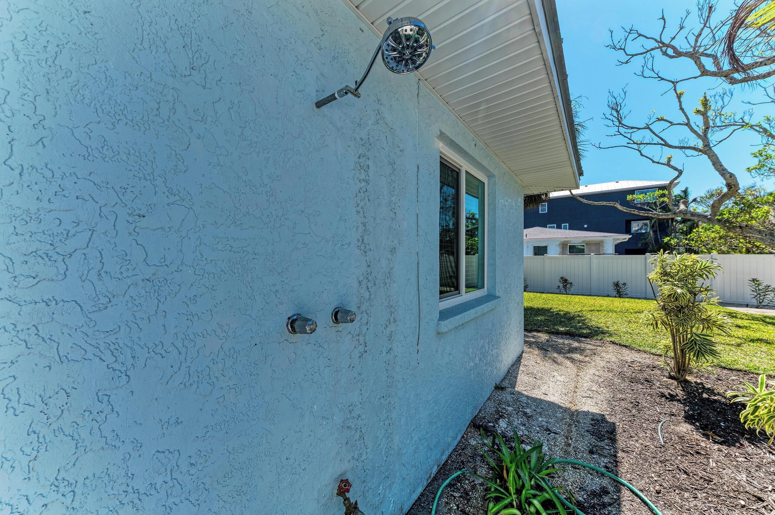 A house with a light blue exterior, a window, and a small garden with plants and a hose.