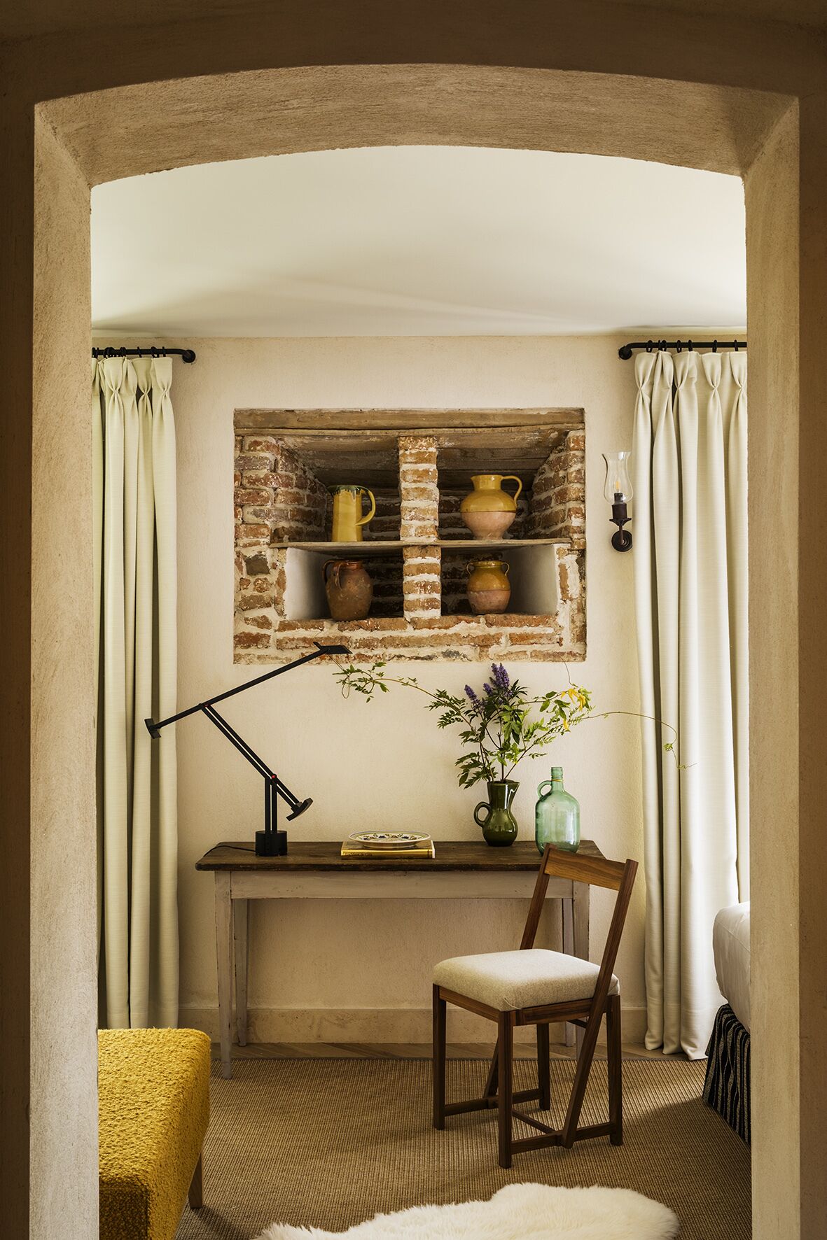 A cozy room with a brick shelf, a desk, a chair, and a yellow armchair.