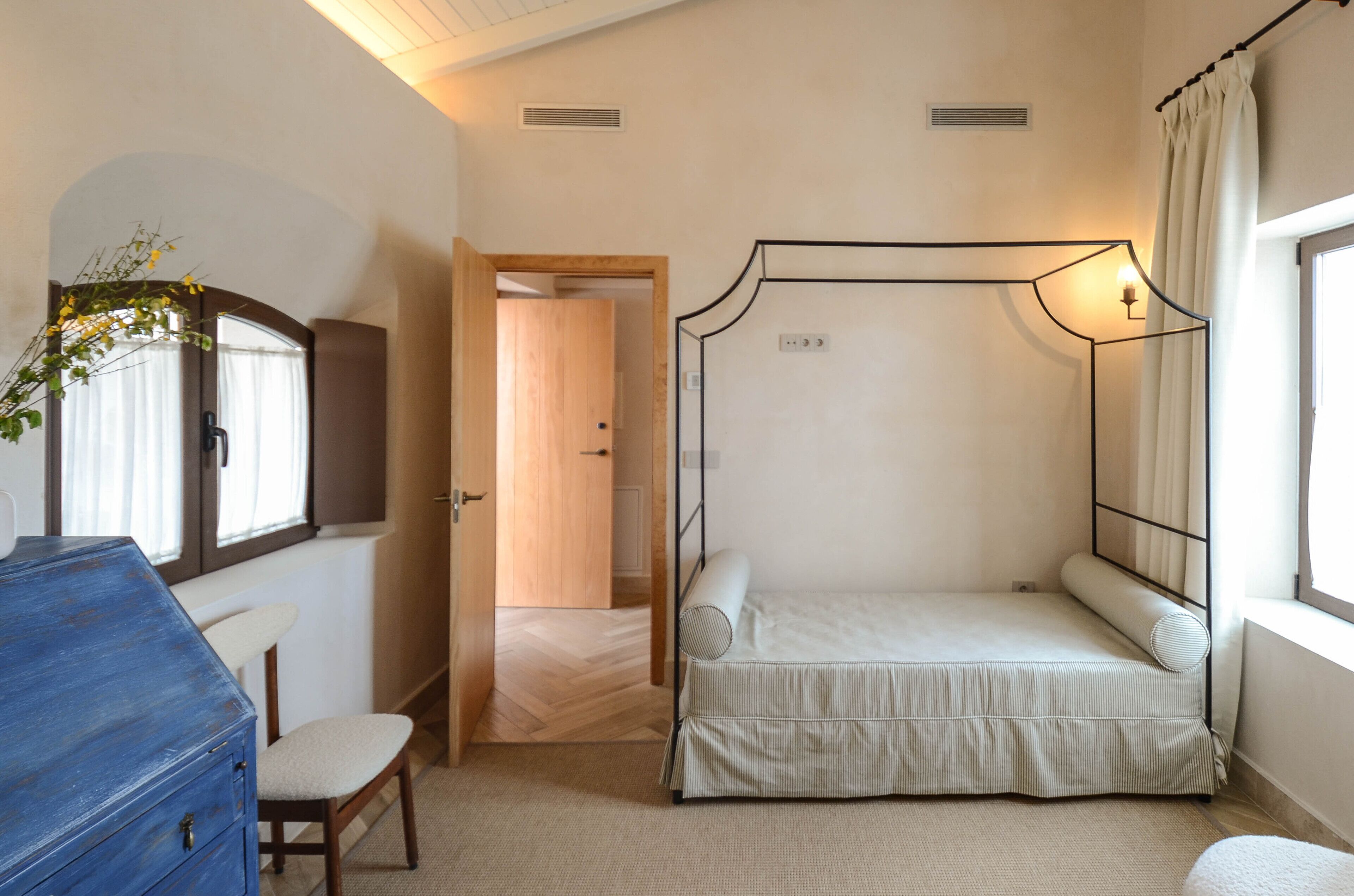 Un dormitorio con cama con dosel, cómoda, silla y ventana con cortinas.