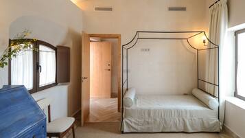 Un dormitorio con cama con dosel, cómoda, silla y ventana con cortinas.