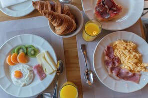 Une table de petit-déjeuner avec des assiettes contenant des œufs, du jambon, des kiwis, des tranches d’orange et des croissants, accompagnées de verres de jus d’orange.