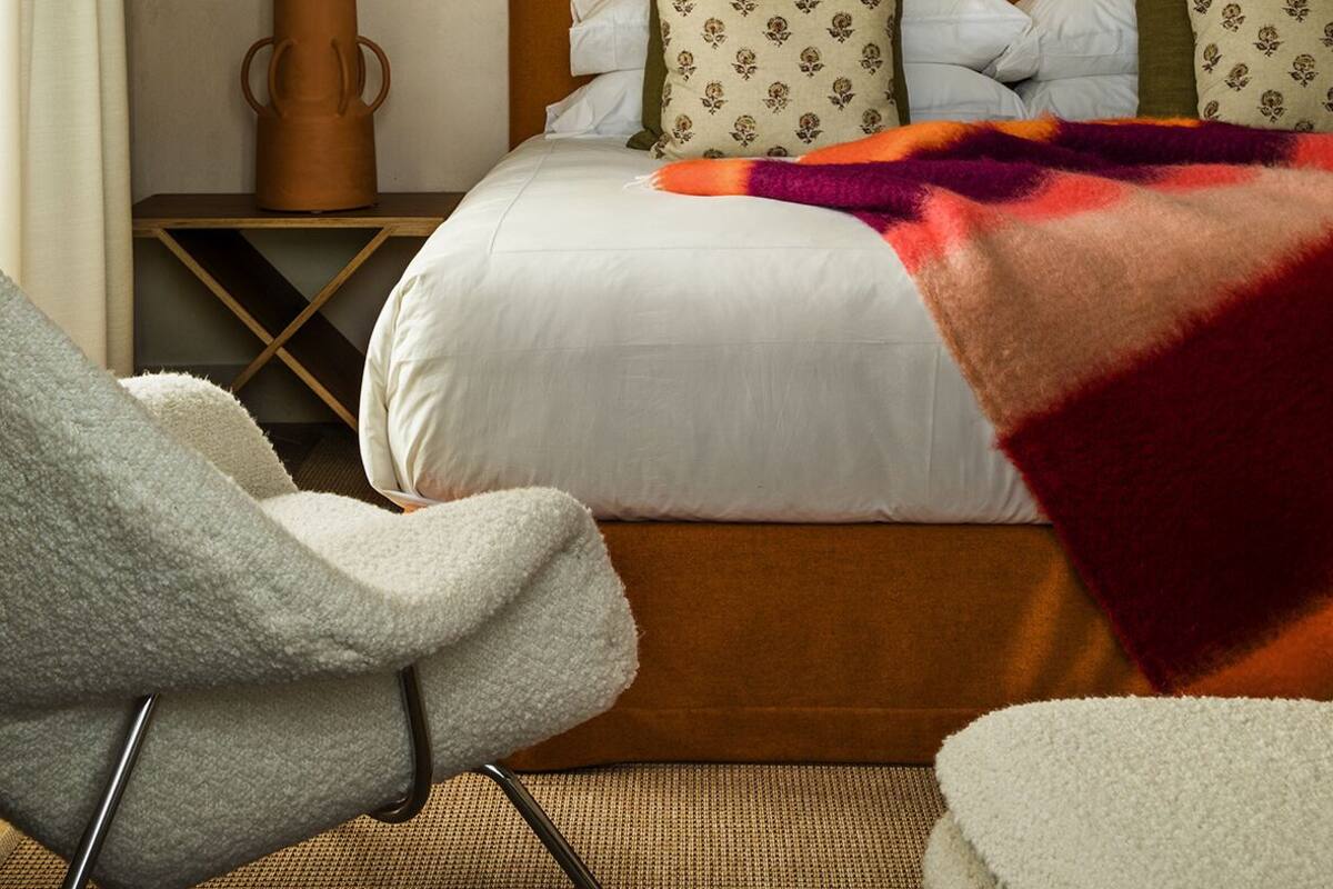 A hotel room with a large bed, a nightstand with a lamp, a decorative wall piece, and a chair with a blanket.