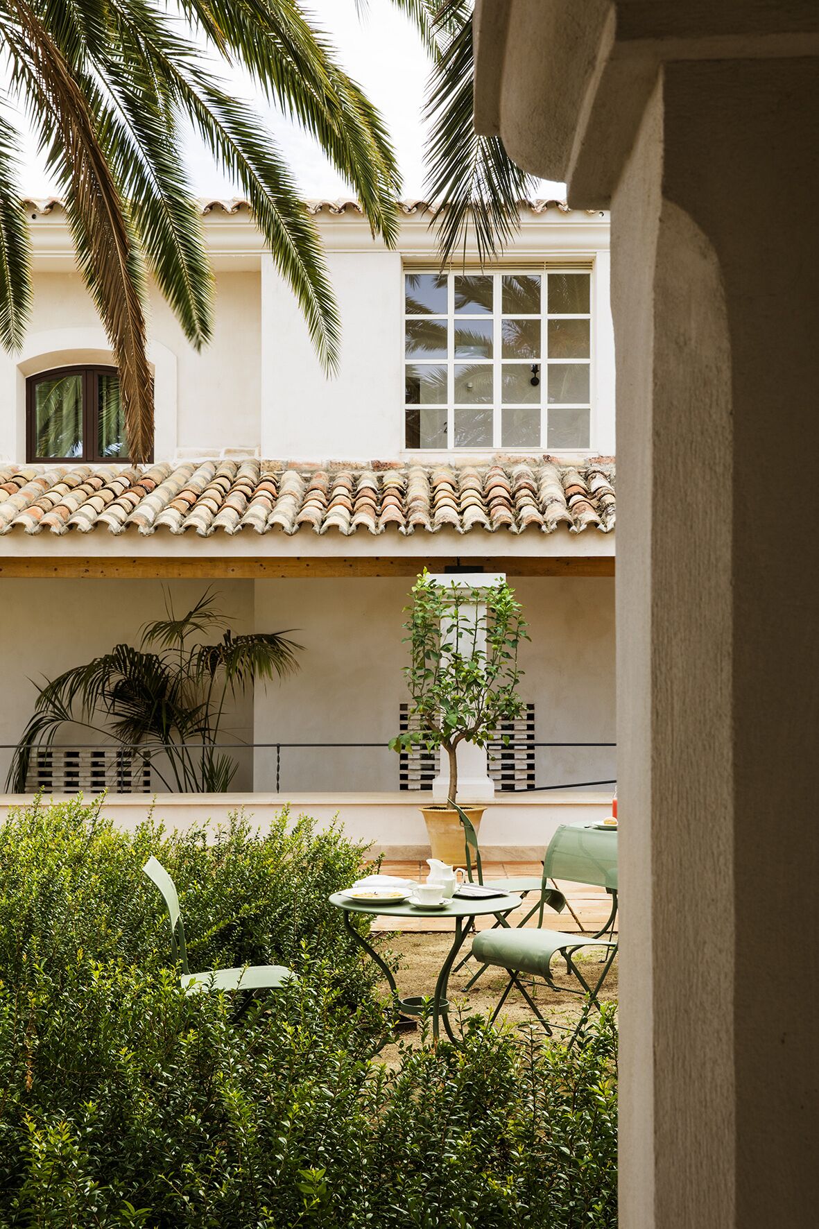 Une cour avec un toit en tuiles, une table avec des chaises et un pot de fleurs.