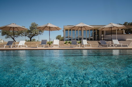 Una piscina al aire libre, sombrillas, sillones reclinables de piscina