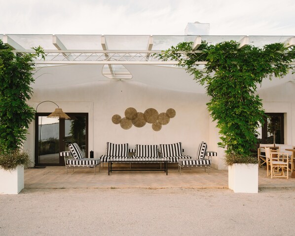 Un área de estar al aire libre techada con un sofá a rayas blancas y negras, una mesa de comedor con sillas y un objeto decorativo en la pared.
