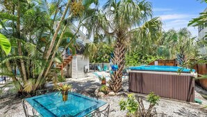 Un jardin avec une table en verre, un jacuzzi et diverses plantes tropicales.