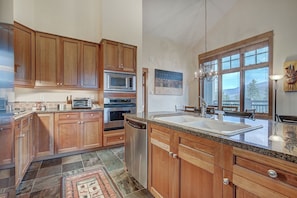 A kitchen with wooden cabinets, stainless steel appliances, a large island with a sink, and a view of mountains through the windows.