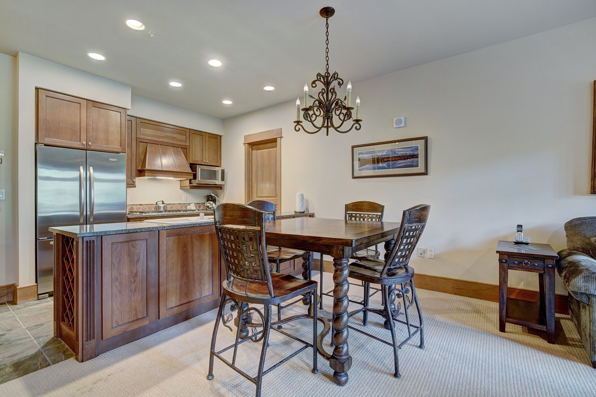 A kitchen with wooden cabinets, a stainless steel refrigerator, a microwave, and a dining table with four chairs.