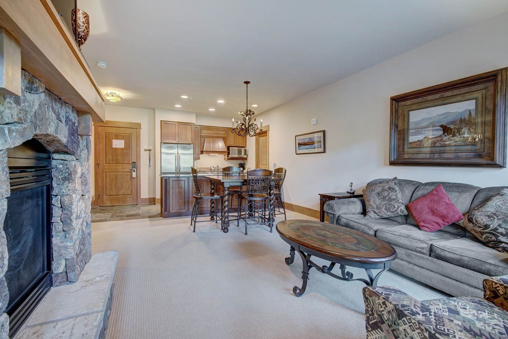 A spacious living area with a stone fireplace, a dining table with chairs, a sofa, and a large painting on the wall.