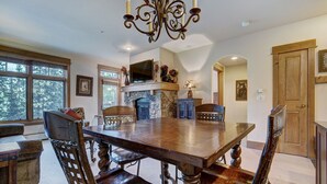 Une salle à manger spacieuse avec une grande table en bois, des chaises élégantes, une cheminée en pierre et un lustre.