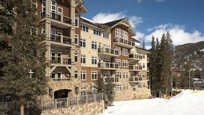 Un hôtel à plusieurs étages, doté de balcons et d’une façade en pierre, avec une piste de ski en arrière-plan.