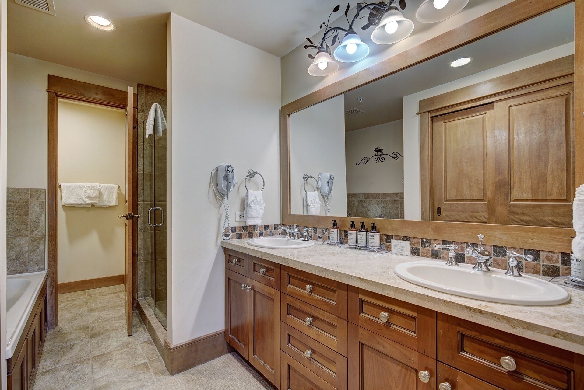 A bathroom with two sinks, wooden cabinets, a large mirror, and a shower area.