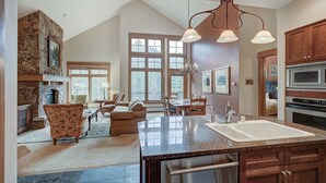 A spacious kitchen with a large island, granite countertops, and modern appliances. There are multiple windows providing natural light and a view of the outdoors.