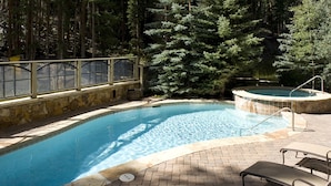 A swimming pool with a stone border, a hot tub, and lounge chairs.