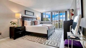 Une chambre d’hôtel moderne équipée d’un lit, de tables de chevet, d’un bureau avec un ordinateur et offrant une vue sur l’extérieur.