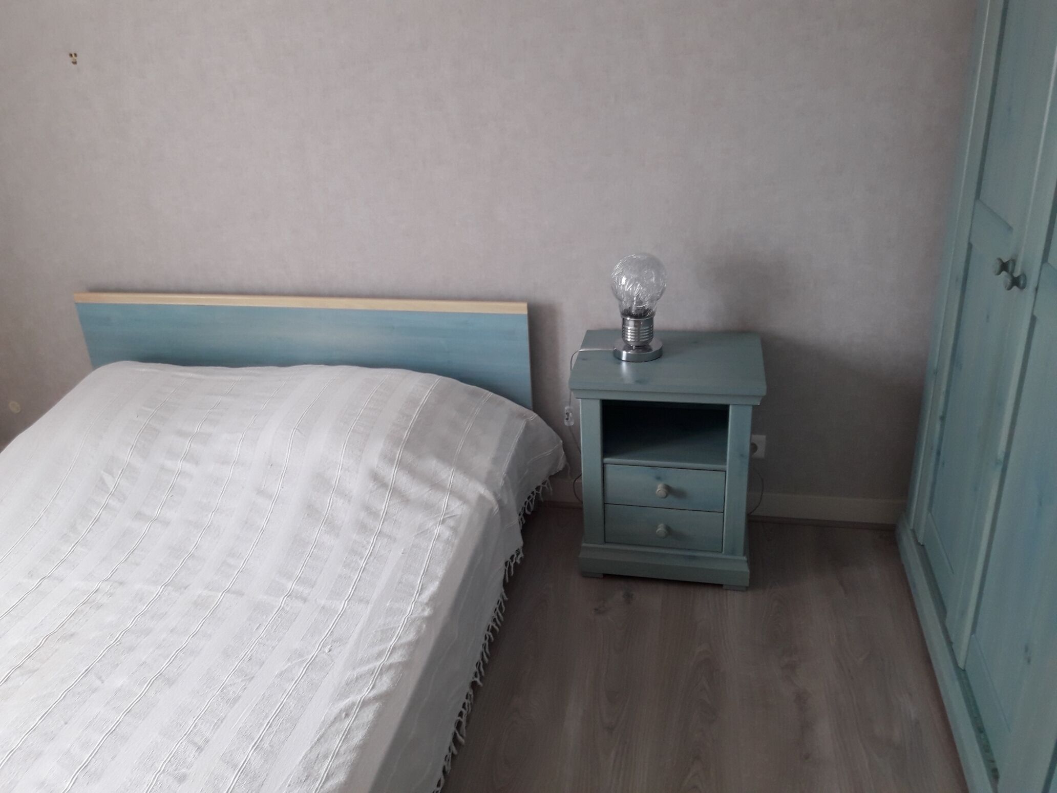Un dormitorio con cama, mesita de noche con lámpara y armario.