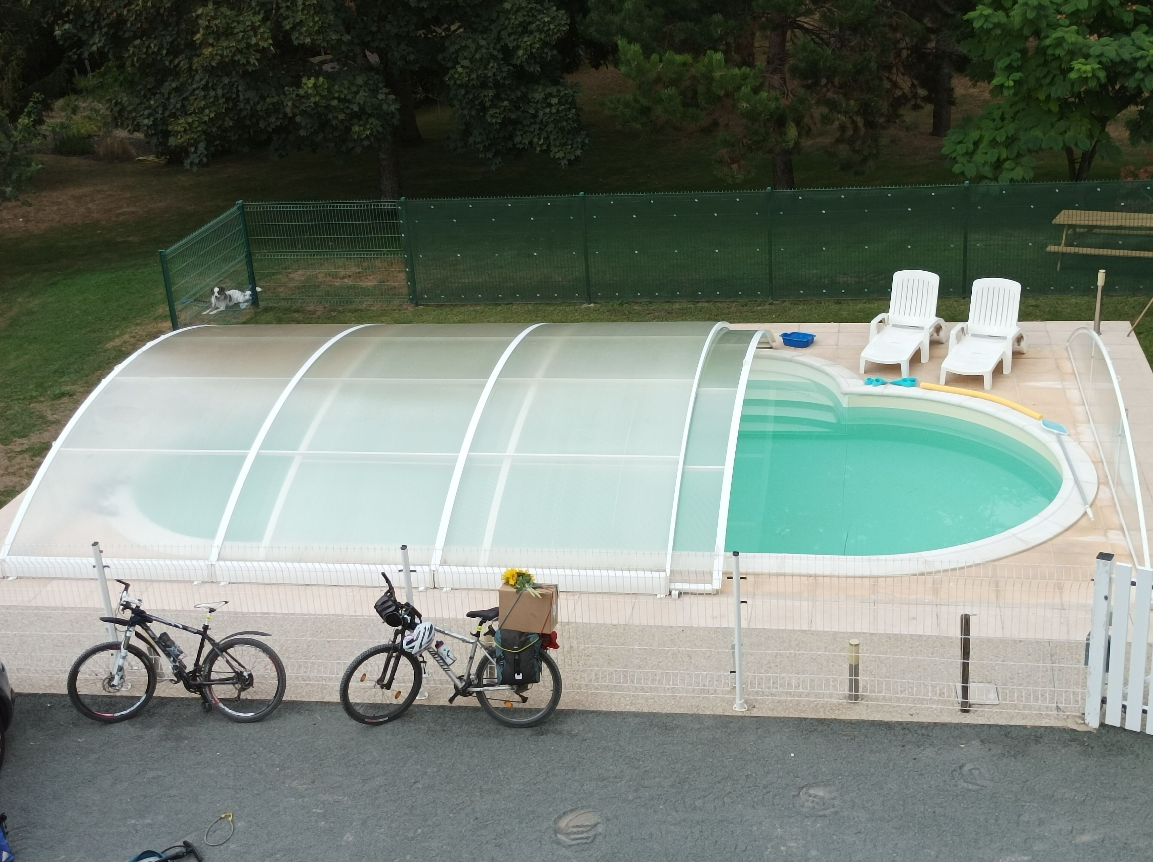 A swimming pool with a cover, surrounded by a fence, and a few bicycles parked nearby.