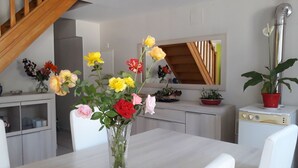 A modern kitchen with white cabinetry, a wooden staircase, and a vase of flowers on the dining table.
