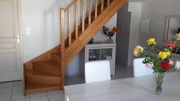 Una escalera con barandillas de madera que conduce a un piso superior. En primer plano, una consola blanca con un florero.