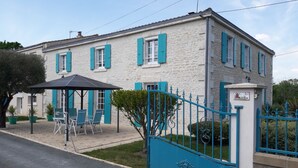 A two-story stone house with blue shutters, a covered patio with chairs, and a gated entrance.