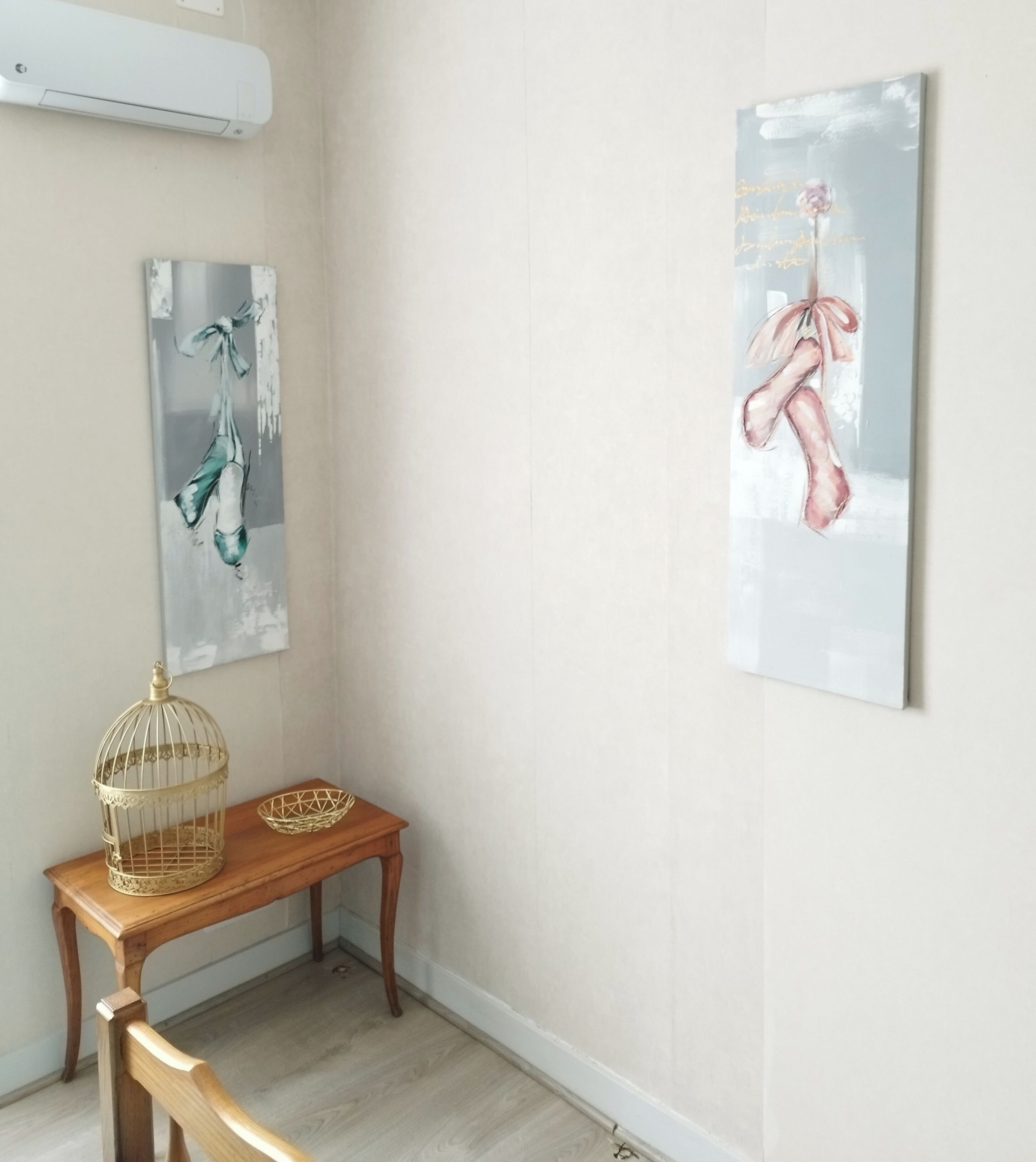 Een gang met een houten bankje, een decoratieve vogelkooi en twee kunstwerken in lijsten aan de muur.