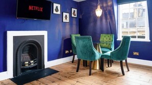 Una stanza con una parete blu, un camino, una televisione che mostra 'NETFLIX' e una finestra con vista sugli edifici.