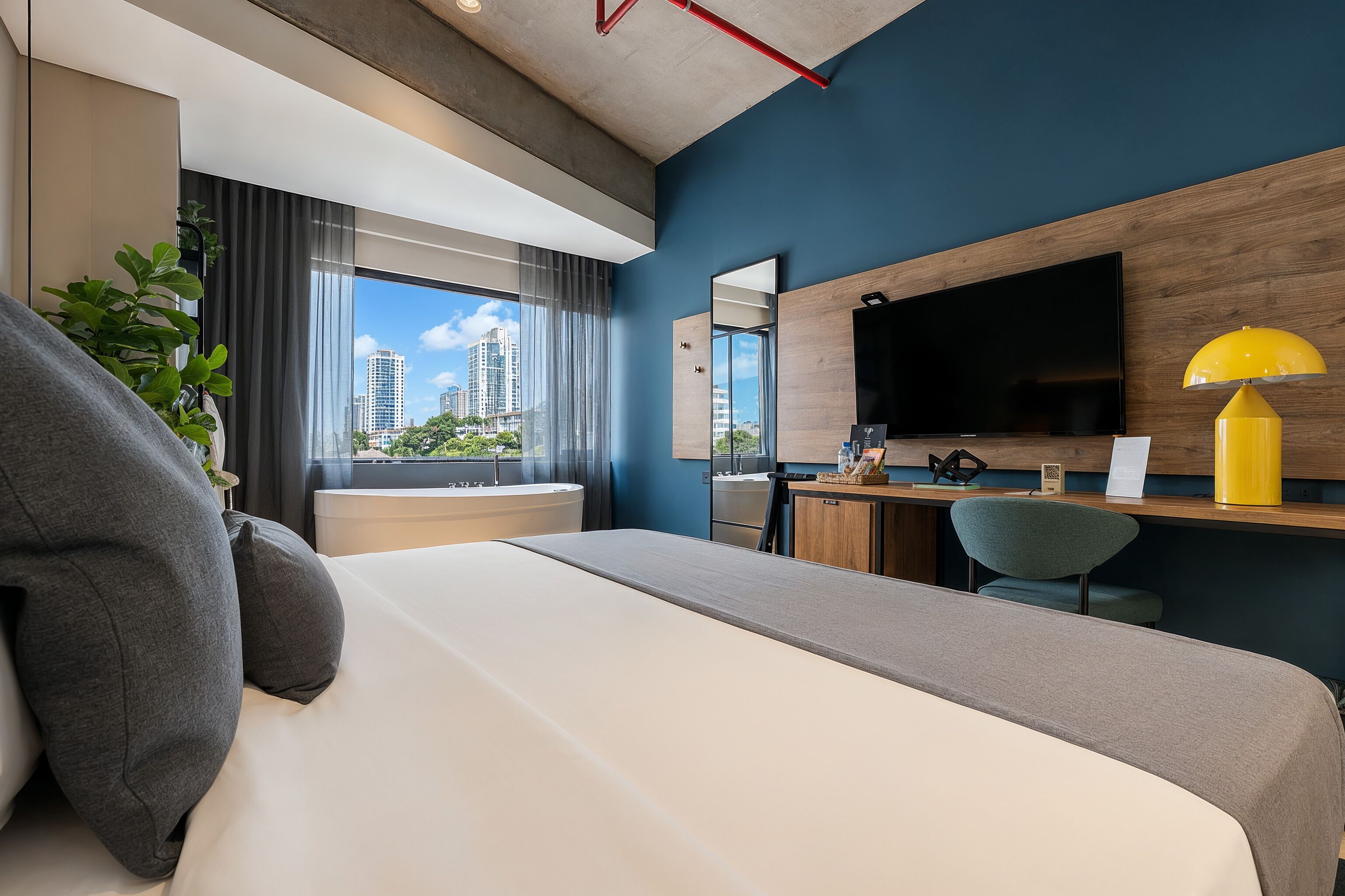 Une chambre d’hôtel moderne équipée d’un lit, d’un bureau, d’une chaise, d’une télévision et d’une fenêtre donnant sur la ville.