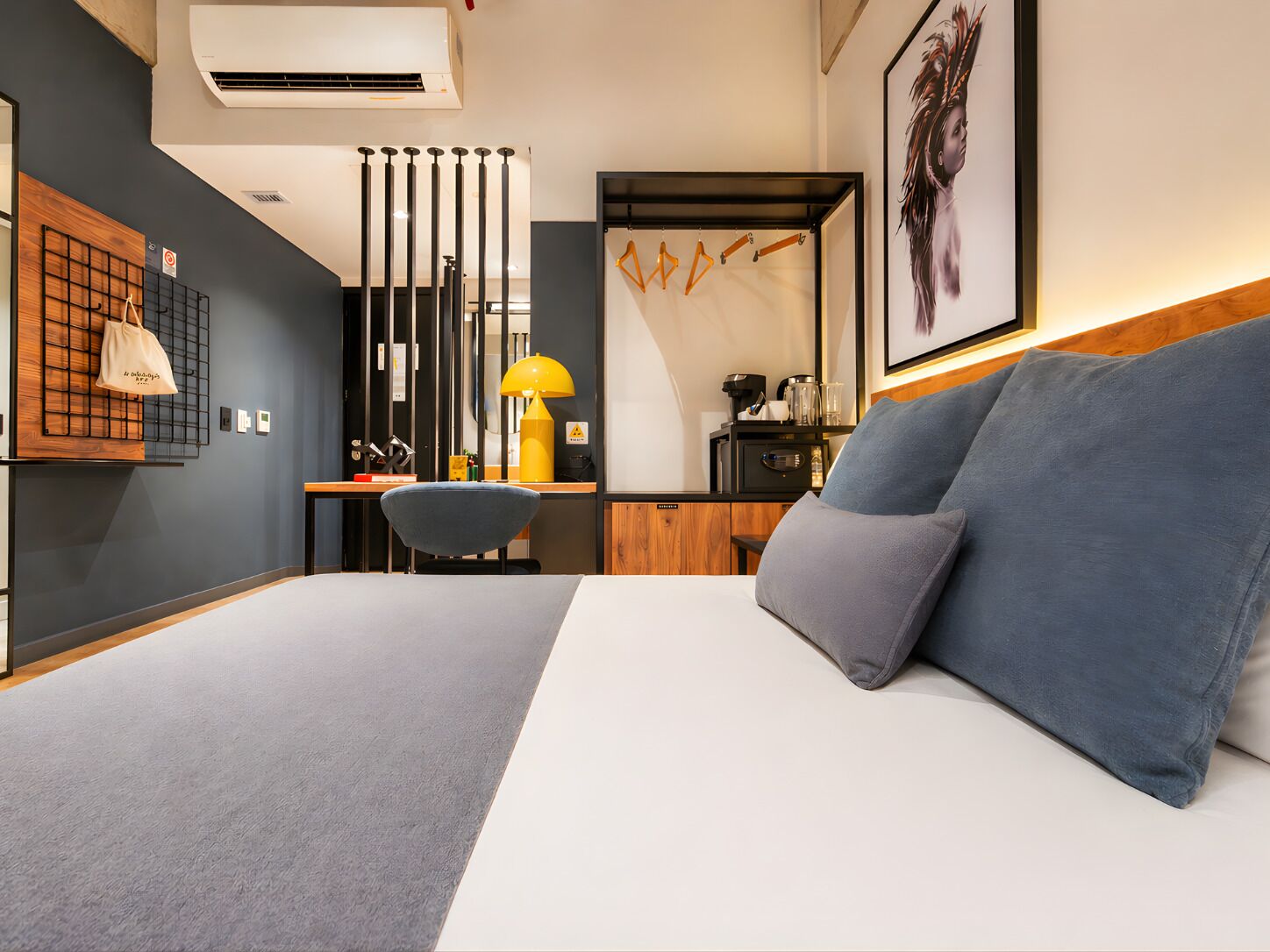 Una habitación de hotel moderna con cama, escritorio, silla, lámpara y un cuadro en la pared.