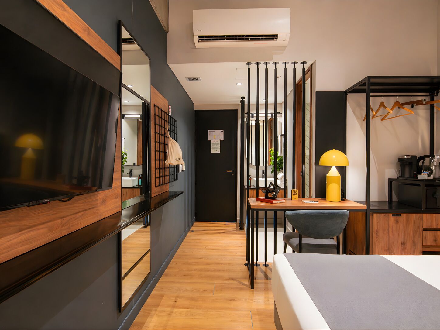 A modern hotel room with a bed, desk, chair, and a mirror.